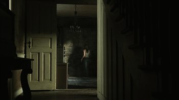 Movie still from “The Texas Chainsaw Massacre” (2003), directed by Marcus Nispel – A person standing in a dark room with smoke coming out of a door; Wide shot, High angle
