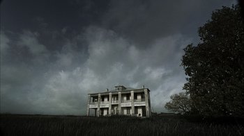 Movie still from “The Texas Chainsaw Massacre” (2003), directed by Marcus Nispel – An old abandoned house in a field under a cloudy sky; Extreme Wide shot, Low angle