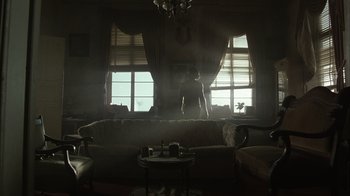 Movie still from “The Texas Chainsaw Massacre” (2003), directed by Marcus Nispel – A person standing in a room with a couch and a table in front of a window; Extreme Wide shot, Low angle