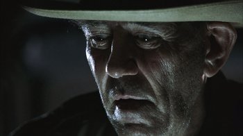 Movie still from “The Texas Chainsaw Massacre” (2003), directed by Marcus Nispel – An old man with a hat and a serious look on his face; Extreme Close Up shot, Low angle