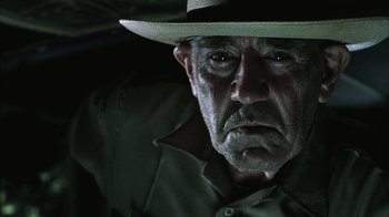Movie still from “The Texas Chainsaw Massacre” (2003), directed by Marcus Nispel – An older man wearing a hat and a green shirt; Close Up shot, Low angle
