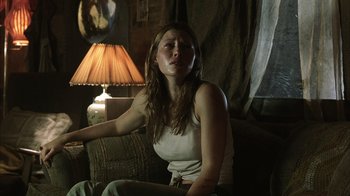 Movie still from “The Texas Chainsaw Massacre” (2003), directed by Marcus Nispel – A woman sitting on top of a couch next to a lamp; Medium shot, Low angle
