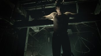 Movie still from “The Texas Chainsaw Massacre” (2003), directed by Marcus Nispel – A man standing in the dark with his arms outstretched; Medium shot, Low angle