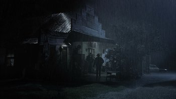 Movie still from “The Texas Chainsaw Massacre” (2003), directed by Marcus Nispel – A man standing in front of a house in the rain; Extreme Wide shot, Low angle