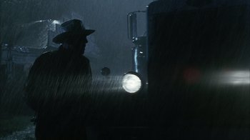 Movie still from “The Texas Chainsaw Massacre” (2003), directed by Marcus Nispel – A man wearing a hat standing in the rain; Medium shot, Low angle