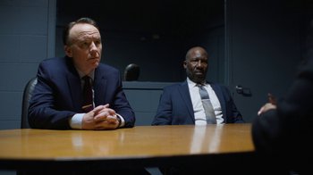 Movie still from “Full Circle” (2023), directed by Steven Soderbergh – Two men in suits sitting at a wooden table; Medium shot, Low angle