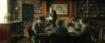 Movie still from “The Theory of Everything” (2014), directed by James Marsh – A group of people sitting at a table in a room; Medium shot, Over the shoulder angle