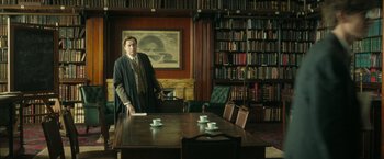 Movie still from “The Theory of Everything” (2014), directed by James Marsh – A man standing in front of a table in a library; Wide shot, Low angle