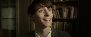 Movie still from “The Theory of Everything” (2014), directed by James Marsh – A young man smiling with a book shelf in the background; Close Up shot, Over the shoulder angle