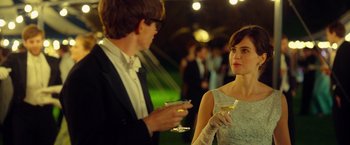 Movie still from “The Theory of Everything” (2014), directed by James Marsh – A man and a woman standing next to each other holding wine glasses; Medium shot, Over the shoulder angle