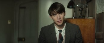 Movie still from “The Theory of Everything” (2014), directed by James Marsh – A man in a suit and tie sitting in front of a lamp; Close Up shot, Over the shoulder angle