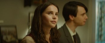 Movie still from “The Theory of Everything” (2014), directed by James Marsh – A young woman looking to her left while standing next to a man; Close Up shot, Over the shoulder angle