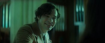 Movie still from “The Theory of Everything” (2014), directed by James Marsh – A young man smiling for the camera in a green room; Close Up shot, Over the shoulder angle