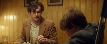 Movie still from “The Theory of Everything” (2014), directed by James Marsh – A man in a brown jacket holding a glass of wine; Medium shot, Over the shoulder angle