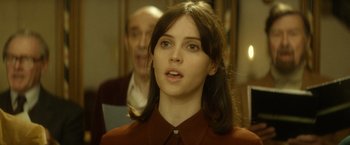 Movie still from “The Theory of Everything” (2014), directed by James Marsh – A young woman in a red shirt is looking at the camera; Close Up shot, Over the shoulder angle