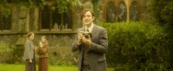 Movie still from “The Theory of Everything” (2014), directed by James Marsh – A man in a suit and tie holding a camera; Medium shot, High angle