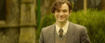 Movie still from “The Theory of Everything” (2014), directed by James Marsh – A man in a suit and tie smiling for the camera; Medium shot, High angle