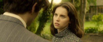 Movie still from “The Theory of Everything” (2014), directed by James Marsh – A young woman looking at the camera while a man looks at her; Close Up shot, Over the shoulder angle