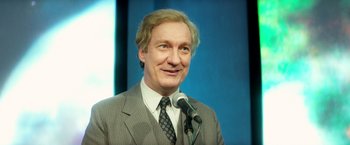 Movie still from “The Theory of Everything” (2014), directed by James Marsh – A man in a suit and tie is speaking at a microphone; Close Up shot, High angle