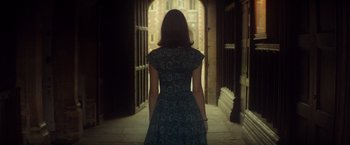 Movie still from “The Theory of Everything” (2014), directed by James Marsh – A woman in a dress is walking down a hallway; Medium shot, Over the shoulder angle