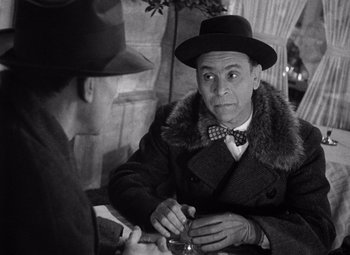 Movie still from “The Third Man” (1949), directed by Carol Reed – A man wearing a hat and a coat is playing cards; Medium shot, Over the shoulder angle