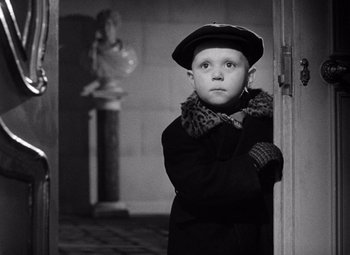Movie still from “The Third Man” (1949), directed by Carol Reed – A young boy in a coat and hat standing in front of a doorway; Medium shot, Over the shoulder angle