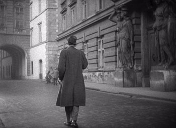 Movie still from “The Third Man” (1949), directed by Carol Reed – An older man walking down the street in a coat and hat; Wide shot, Low angle