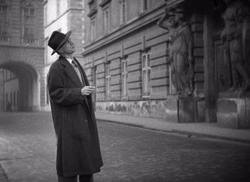 Movie still from “The Third Man” (1949), directed by Carol Reed – An older man wearing a coat and a hat standing on the street; Wide shot, Low angle