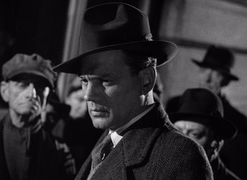 Movie still from “The Third Man” (1949), directed by Carol Reed – A man wearing a hat standing in front of a group of people; Close Up shot, Low angle