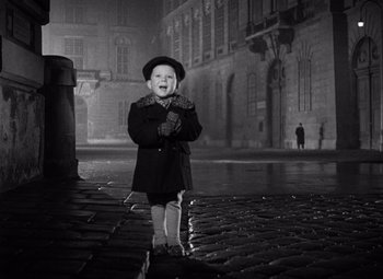 Movie still from “The Third Man” (1949), directed by Carol Reed – A little boy wearing a coat and hat standing on the sidewalk; Wide shot, High angle