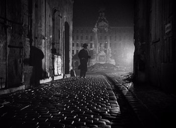Movie still from “The Third Man” (1949), directed by Carol Reed – A man standing on a brick walkway in a dark city; Wide shot, Low angle
