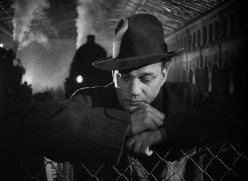 A black and white photo of a man leaning on a fence