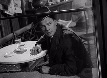 Movie still from “The Third Man” (1949), directed by Carol Reed – A black and white photo of a man sitting at a table; Medium shot, High angle