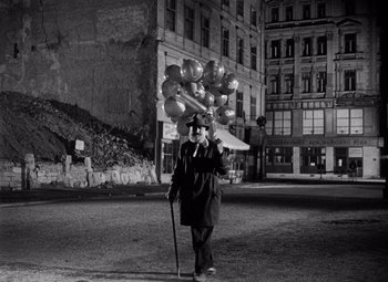 Movie still from “The Third Man” (1949), directed by Carol Reed – An old man walking in the middle of a street with a bunch of balloons on his head; Wide shot, Low angle