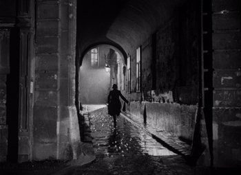 Movie still from “The Third Man” (1949), directed by Carol Reed – A person walking down a street in the rain; Wide shot, High angle