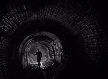 Movie still from “The Third Man” (1949), directed by Carol Reed – A man standing inside of an old brick tunnel; Wide shot, Low angle