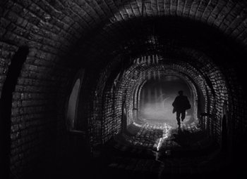 Movie still from “The Third Man” (1949), directed by Carol Reed – A man walking in a tunnel with smoke coming from it; Wide shot, Low angle