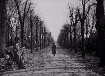 An old photo of a woman walking down a tree lined street