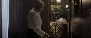 Movie still from “The Thirteenth Floor” (1999), directed by Josef Rusnak – An older man in a white dress shirt and black pants is standing in front of a clock; Medium shot, Low angle