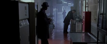 Movie still from “The Thirteenth Floor” (1999), directed by Josef Rusnak – A man in a black coat and a black hat is standing in a kitchen; Wide shot, High angle