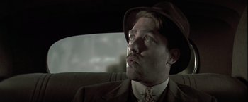 Movie still from “The Thirteenth Floor” (1999), directed by Josef Rusnak – A man in a suit and hat sitting in the back seat of a car; Close Up shot, Low angle