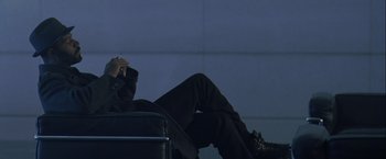 Movie still from “The Thirteenth Floor” (1999), directed by Josef Rusnak – A man sitting on a chair with his legs crossed; Medium shot, Low angle