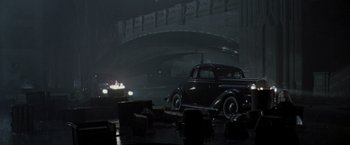 Movie still from “The Thirteenth Floor” (1999), directed by Josef Rusnak – An old car is parked on the side of the road in the rain; Extreme Wide shot, High angle