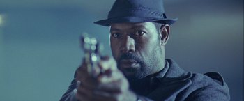 Movie still from “The Thirteenth Floor” (1999), directed by Josef Rusnak – A man in a fedora holding a gun in his hand; Close Up shot, Low angle