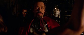 Movie still from “The Three Musketeers” (1993), directed by Stephen Herek – A person with a beard wearing a red cape; Close Up shot, Over the shoulder angle