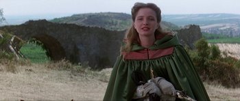 Movie still from “The Three Musketeers” (1993), directed by Stephen Herek – A woman in a green and red cape standing on top of a hill; Medium shot, Over the shoulder angle
