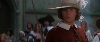 Movie still from “The Three Musketeers” (1993), directed by Stephen Herek – A man with a hat and a sword in front of a group of people; Close Up shot, Low angle