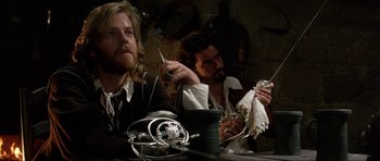 Movie still from “The Three Musketeers” (1993), directed by Stephen Herek – Two men sitting at a table in front of a candle; Medium shot, Over the shoulder angle