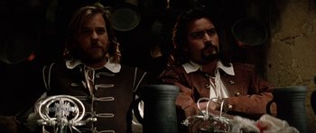 Movie still from “The Three Musketeers” (1993), directed by Stephen Herek – A couple of men sitting next to each other in a room; Medium shot, Low angle