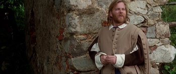 Movie still from “The Three Musketeers” (1993), directed by Stephen Herek – A man with long hair and a beard standing next to a stone wall; Medium shot, Over the shoulder angle